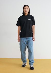 Czarny bawełniany t-shirt z logo "CARRHARTT", połączony z jasnoniebieskimi dżinsami. Posiada luźny krój i sportowe czarne sneakersy.