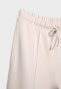 Světle béžové tepláky s elastickým pasem, šňůrkovým uzavíráním a bočními kapsami, s jemnou texturou a minimalistickým designem.