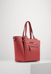 Borsa a mano in pelle rossa con doppi manici superiori, due tasche frontali e dettagli in metallo. Finitura texturizzata con design strutturato.