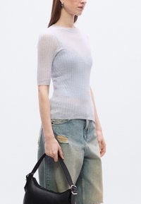 Ανοιχτό μπλε ριμπ πλεκτό τοπ με κοντά μανίκια, σε συνδυασμό με φθαρμένο μπλε τζιν. Μαύρη τσάντα χειρός, συνολικό καθημερινό στυλ.