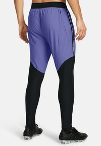 Lila und schwarze Sporthose mit tailliertem Design und elastischem Bund, mit einem seitlichen Logodetail entlang der Nähte.