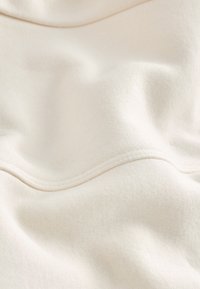 Light beige fabric with a smooth texture, featuring subtle seams and folds. The material appears soft and slightly stretchy.