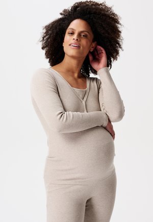 Beige geribbelde zwangerschaps-top met een diepe V-hals en knoopdetails, gecombineerd met bijpassende op maat gemaakte broek, die de zachte textuur en comfortabele pasvorm benadrukt.