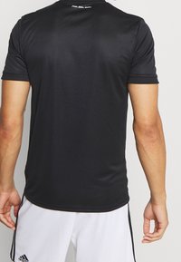 Maglietta atletica nera a maniche corte con una texture liscia. Presenta il testo bianco "Mia san mia" nell'area dietro il collo. Design slim fit.