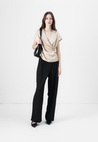 Beige drapertopp med korte ermer, kombinert med svarte vide bukser. En svart håndveske og spisse sko fullfører antrekket.