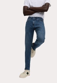 Jeans blu scuro slim fit, realizzati in denim. Presentano cinque tasche, passanti per la cintura e aree leggermente sbiadite. Abbinati a sneakers beige.