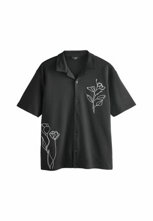 Chemise noire à manches courtes avec boutons et col, ornée d'un motif floral minimaliste blanc en lignes sur la poitrine et le bas du côté.