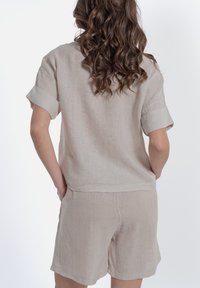 Completo in lino di un beige chiaro, composto da una maglietta a maniche corte con maniche arrotolate e pantaloni shorts abbinati, caratterizzati da un fit casual e un tessuto testurizzato.