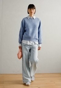 Light blue knitted sweater over a white and blue striped shirt, paired with light wash wide-leg jeans and a light pink bag.