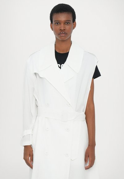 Λευκό παλτό με υπερμεγέθη γιακά, διπλό κούμπωμα μπροστά και ζώνη στη μέση. Έχει κοντά μανίκια και λείο, υφασμάτινο ύφασμα.