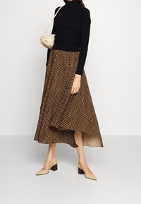 Zwarte geribbelde coltrui gecombineerd met een bruin geblokt plooirok tot de knie en beige blokhak schoenen. Een tan handtas maakt de outfit compleet.