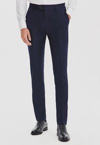Granatowe formalne spodnie o dopasowanym kroju, z gładką teksturą, czterema kieszeniami oraz zapięciem na guzik i zamek. Noszone z czarnymi butami.