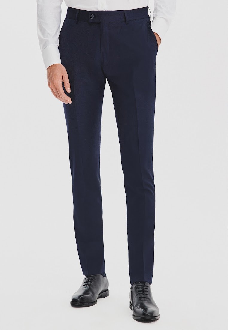 Granatowe formalne spodnie o dopasowanym kroju, z gładką teksturą, czterema kieszeniami oraz zapięciem na guzik i zamek. Noszone z czarnymi butami.