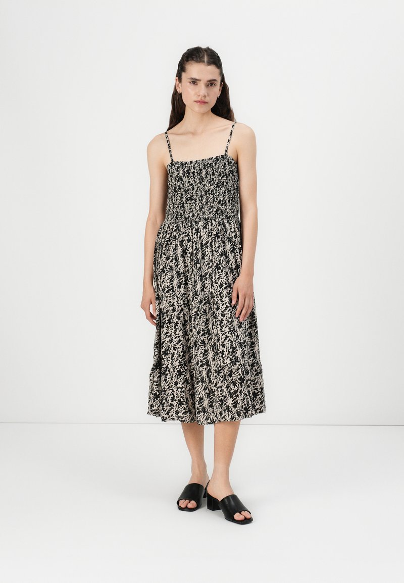 Rochie midi alb-negru, cu model floral, cu bustul elastificat, bretele subțiri și fustă vaporoasă. Asortată cu sandale negre cu talpă plată.