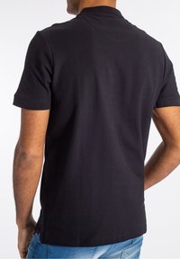 Black polo shirt with a ribbed collar and short sleeves, made from smooth fabric, featuring a side hem accent in red.