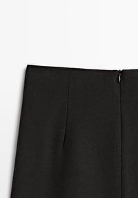 Section de tissu noir avec une couture verticale et une petite languette noire de fermeture éclair sur le côté droit sur fond blanc.