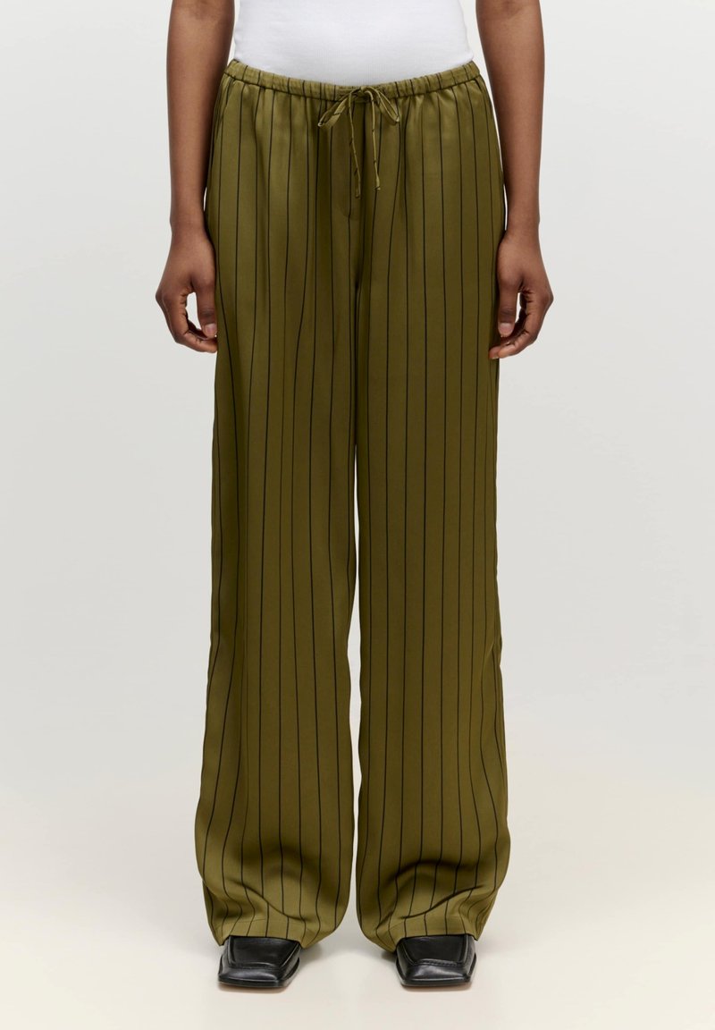 Olijfgroene, wijde broek met verticale zwarte strepen, gemaakt van een gladde stof. Voorzien van een elastische tailleband met een trekkoord.