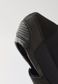 Cizmă neagră tip slip-on, cu un capac elastic texturat, călcâi din cauciuc și cusături întărite pentru durabilitate. Interior neted și design flexibil.