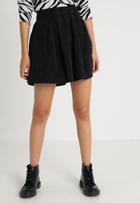 Zwarte corduroy mini-rok met plooien, een hoge tailleband en een gestructureerd oppervlak. Gepaard met zwarte vetercombatlaarzen.