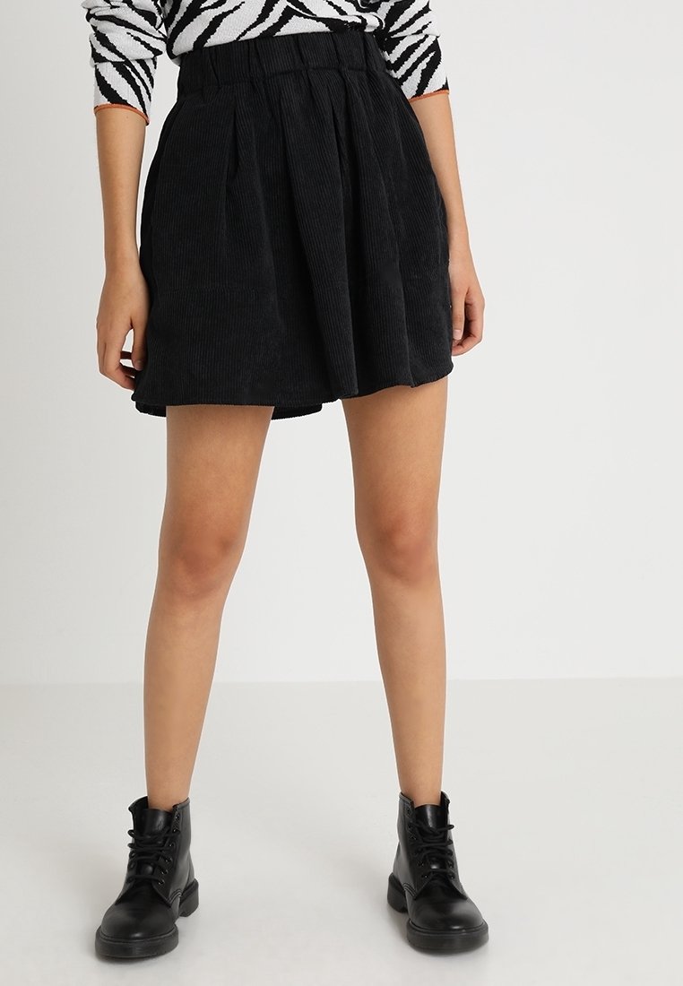 Zwarte corduroy mini-rok met plooien, een hoge tailleband en een gestructureerd oppervlak. Gepaard met zwarte vetercombatlaarzen.