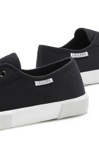 Schwarze Leinensneaker mit weißen Gummisohlen, runden Ösen und einem Markenlabel an der Ferse. Einfaches, flaches Design.