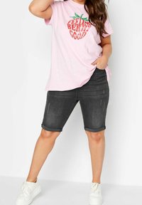 Camiseta rosa con gráfico "FEELING BERRY GOOD" y bermudas de mezclilla oscura. Zapatos deportivos blancos. Conjunto casual de corte relajado.
