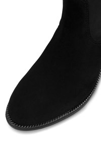 Czarne zamszowe botki za kostkę o gładkiej teksturze, o migdałowym nosku i dekoracyjnym przeszyciu wzdłuż podeszwy. Posiadają wyściełany kołnierz dla wygody.