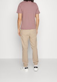 T-shirt bordeaux à manches courtes associé à un pantalon de jogging beige et des baskets blanches avec des accents bleu marine au niveau du talon. Design simple et coupe décontractée.