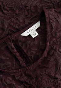 Tummat burgundinväriset tekstuurilla varustetut kankaat, joissa on kukkakuosi, jossa on taitettu kaulus ja valkoinen vaatelappu, jossa lukee "NOELLA S Made in China."