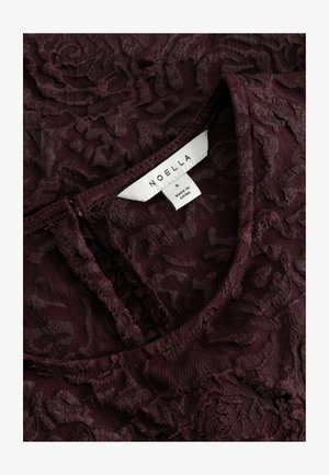 Dark burgundy textured fabric with floral pattern, featuring a folded neckline and a white clothing label reading "NOELLA S Made in China."