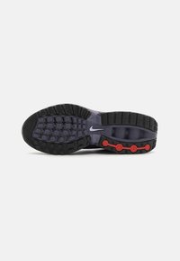 Nike-sko med en svart og lilla teksturert gummisåle, med røde dempende detaljer og synlige mønstre for grep.