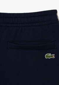 Pantalones de chándal azul marino con cintura elástica, un bolsillo trasero y un pequeño logo bordado de cocodrilo verde con detalles rojos.