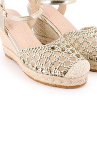Sandalias de cuña con parte superior de tejido dorado, plataforma de paja trenzada beige y detalle de tira. Presentan una suela texturizada para mayor agarre.