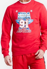 Sweat-shirt rouge présentant un graphique NBA 91 All-Stars avec des accents d'étoiles bleues et blanches. Fabriqué en tissu texturé avec des manches longues.