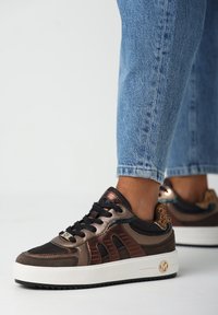 Bruine en zwarte sneakers met metallic accenten, gestructureerde stof, een patroon op de hak en een witte zool met een logo.