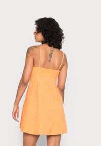 Vestido mini laranja texturizado com alças finas, corpete justo e saia rodada. Apresenta costuras visíveis e um efeito de tecido enrugado.