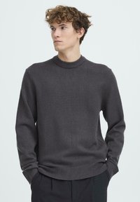 Szürke kötött pulóver kerek nyakkivágással, hosszú ujjakkal, bordázott mandzsettákkal és szegéllyel. Puha tapintású, klasszikus szabású.