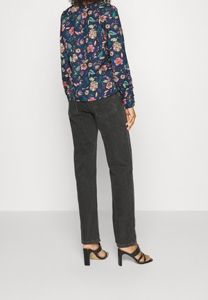 Chemise à manches longues florale bleu marine avec des fleurs colorées, assortie à un jean noir taille haute et des sandales à talons noires.