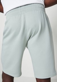 Pantaloni sportivi verde chiaro con vita elasticizzata, texture liscia e design aderente, caratterizzati da cuciture lungo le cuciture.