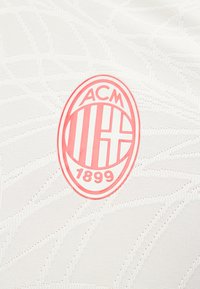 Το λογότυπο της ποδοσφαιρικής ομάδας AC Milan με κόκκινο σε λευκό υφασμάτινο φόντο με αχνά διαγώνια μοτίβα.