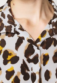 Leopardskinnad skjorta med en ljusgrå bakgrund, bruna och gula fläckar, samt en klassisk krage med en vit knapprad.