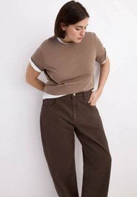 Brązowa bluzka z krótkim rękawem z białą podszewką, zestawiona z ciemnobrązowymi, szerokimi spodniami. Tkanina wydaje się miękka, o luźnym kroju.