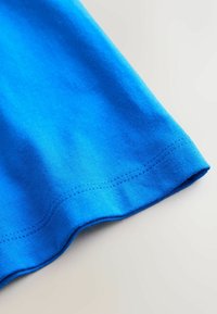 Blue cotton T-shirt with ribbed texture, curved hemline, and double-stitched details along the bottom edge. Smooth finish and vibrant color.