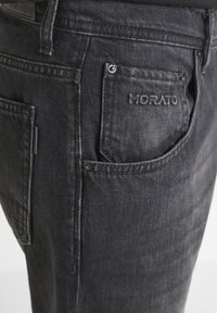 Los pantalones vaqueros de mezclilla negra tienen un ajuste ajustado, costuras visibles, un bolsillo con la marca "MORATO" estampada y acentos de textura desgastada.