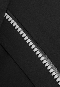 Schwarzer Stoff mit einem kontrastierenden weißen Reißverschluss, der kleine Zähne und einen glatten Schließmechanismus aufweist und eine matte Oberfläche hat.