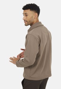 Pullover in pile marrone con colletto e maniche lunghe. Texture liscia, design minimal e silhouette attillata.