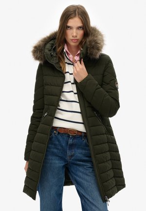 Legergroene pufferjas met een met bont afgewerkte capuchon, voorzien van horizontale stiksels, met ritszakken en een getailleerd silhouet. Gedragen over een gestreept sweater.