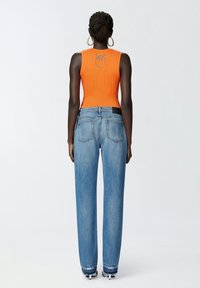 Top sin mangas naranja con canalé y un logo en la parte posterior, combinado con jeans de pierna ancha en azul claro con dobladillo deshilachado y bolsillos traseros.