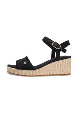 Sandalo con zeppa nero, suola piatta intrecciata, cinturino alla caviglia con fibbia dorata e piccolo logo decorativo dorato sulla fascia anteriore.