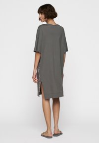 Szara, oversize sukienka t-shirt z lekkiego materiału. Posiada krótkie rękawy, rozcięcia po bokach i luźny krój. Prosty design, bez wzorów ani akcentów.